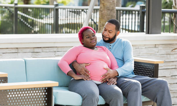 afrikaans-amerikaanse zwangere paarzitting op terrasbank - pregnant couple outside stockfoto's en -beelden
