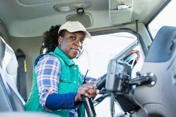African-American woman driving a semi-truck An African-American woman in her 30s sitting in the driver's seat of a semi-truck, looking at the camera. truck driver stock pictures, royalty-free photos & images