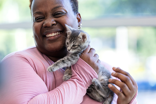 Headshot of a mature African-American woman in her 40s holding a kitten against her cheek, smiling at the camera.