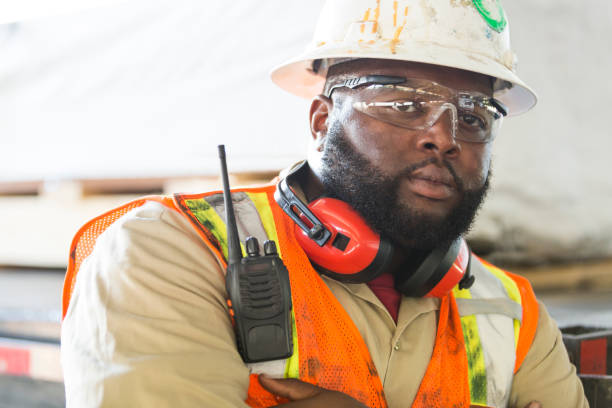 African-American worker in hardhat, reflective vest A mid adult African-American man in his 30s working, wearing a hardhat, safety goggles and reflective vest. He is a construction worker or engineer. His arms are crossed and he has a tough, serious expression on his face. macho stock pictures, royalty-free photos & images
