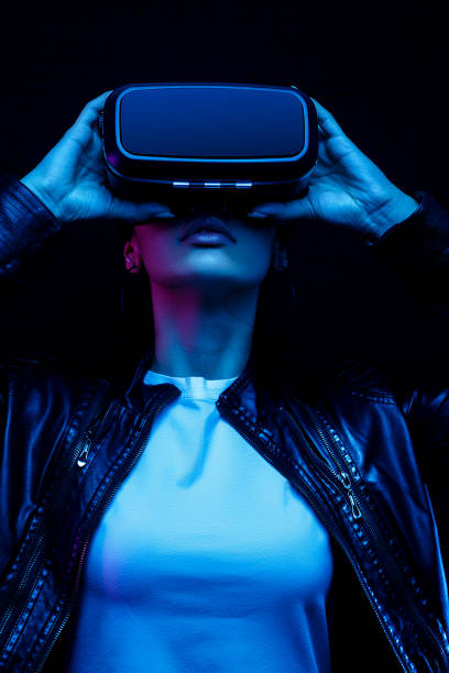African-American young woman in vr glasses watching 360 degree video with a virtual reality headset isolated on a black background in neon light stock photo