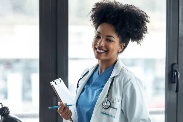 Afro female doctor holding clipboard while looking at camera standing in the consultation. stock photo