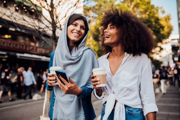 het meisje van afro en haar arabische vriend die telefoon gebruiken en koffie op de straat drinken - walking with coffee stockfoto's en -beelden