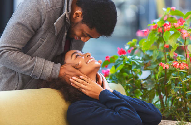 Afro guy in love touching his girlfriend face from behind Black young couple bonding at cafe. Man staying behind woman and touching her face, looking at her eyes, free space falling in love stock pictures, royalty-free photos & images