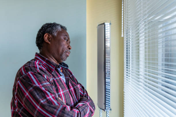 Afro Senior Man Looking Through The Window Photo of Senior Afro-American who is Standing Near the Window and Thoughtfully Looking Through the Window Glass During a Rainy Day. sad old black man stock pictures, royalty-free photos & images