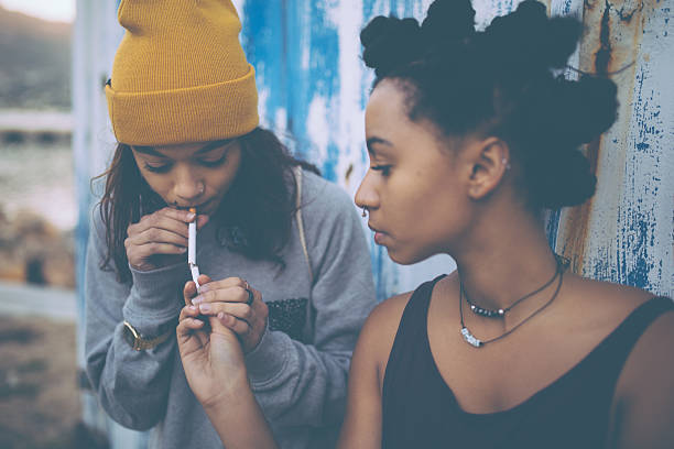 Afro teen lighting a cigarette for her grungy girl friend Afro teen lighting her grungy girl friend's cigarette with another cigarette little girl smoking cigarette stock pictures, royalty-free photos & images