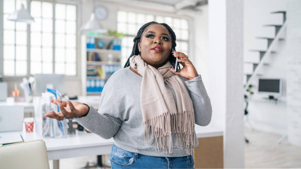 afro kvinna pratar på en smart telefon på jobbet - chubby women office manager bildbanksfoton och bilder