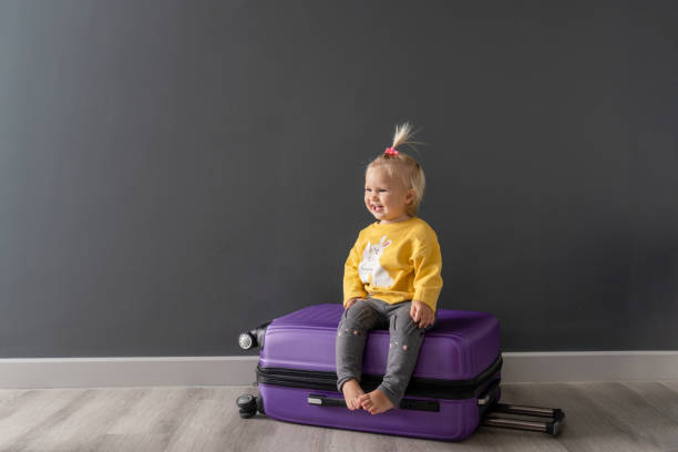 after travel preparation of packing clothes little happy  cute blond child sitting on violet luggage, ready for interesting journey. family travel concept. enough space for text. good background. - foster home bag imagens e fotografias de stock