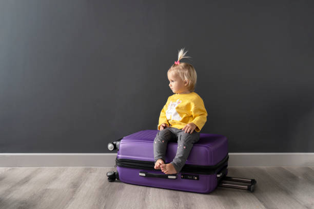 after travel preparation of packing clothes little happy cute blond child sitting on violet luggage, ready for interesting journey. family travel concept. enough space for text. good background. - foster home bag imagens e fotografias de stock