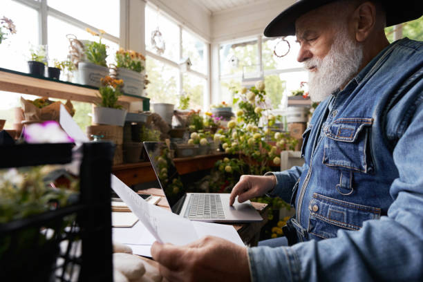 Aged man working with laptop and documents in flower shop stock photo