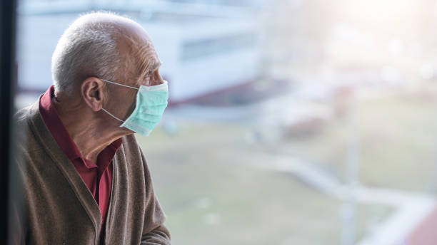 alter rentner mann mit grauen haaren trägt medizinische gesichtsmaske - einsamkeit stock-fotos und bilder