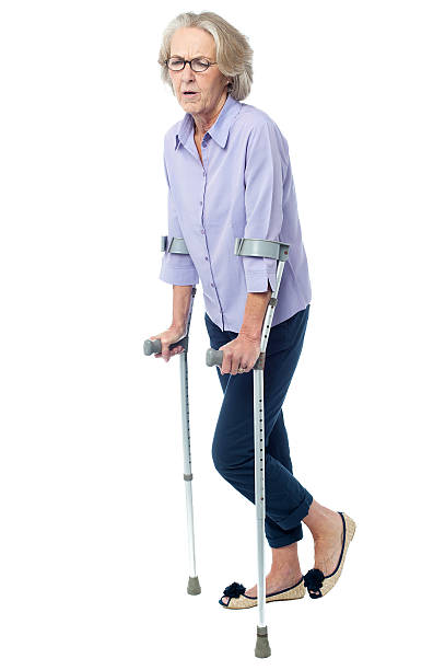 Aged woman in pain walking with crutches stock photo