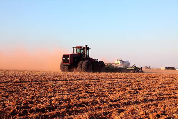 Agriculture: Farmer driving tractor with Fertilizer Tank in plowed field Farmer in tractor putting down anhydrous ammonia in a dusty plowed field. Horizontal image would be good for agriculture use. ammonia stock pictures, royalty-free photos & images
