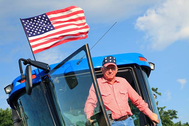 Agriculture: Patriotic American Farmer on Tractor with Flag stock photo