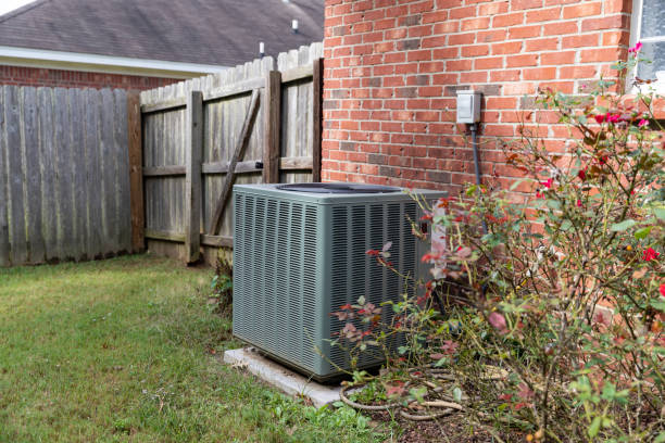 Air conditioner condenser unit sitting next to brick home with fence stock photo