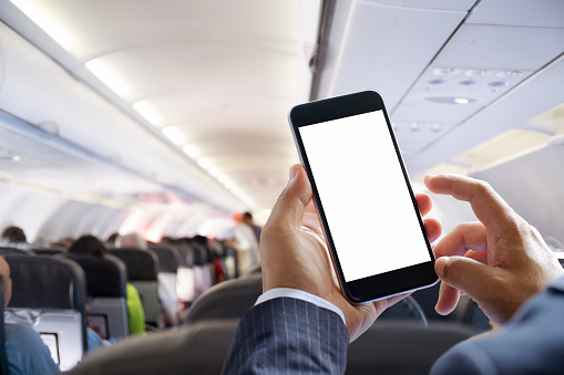 Man's hands holding a smartphone with a white screen on an aeroplane