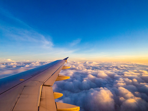 view of the window of an aircraft to a view of the right side wing on a sunrise over the clouds