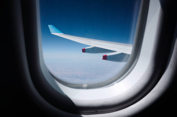 Airplane wing through plane window during flight stock photo