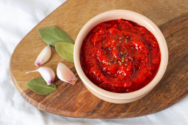 Ajvar in a bowl with garlic and spicy leaves on a wooden board. Serbian or balkan traditional food. Ajvar, balkan traditional sauce in a bowl with garlic and spicy leaves on a wooden board. Serbian traditional food. Close-up. chutney stock pictures, royalty-free photos & images