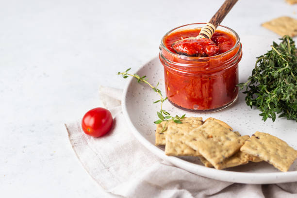 Ajvar (pepper mousse) or pindjur red vegetable spread made from paprika and tomatoes in glass jar on light stone table. Serbian native food. stock photo