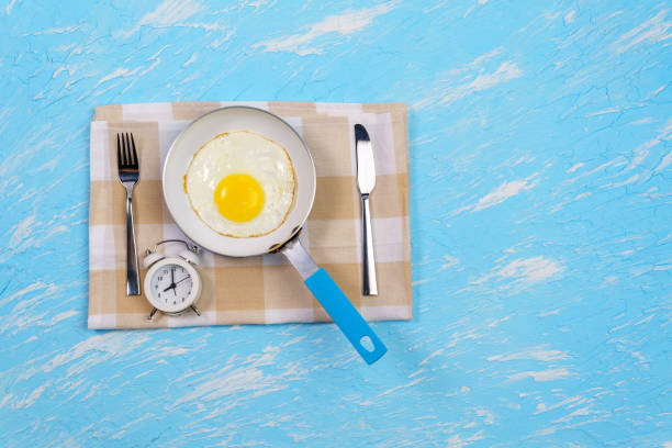 alarm clock and scrambled eggs on a blue background with space to copy. for good morning  soft-boiled egg stock pictures, royalty-free photos & images