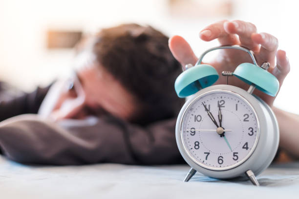 Alarm clock in the morning. Young wakes up in the blurry background. stock photo