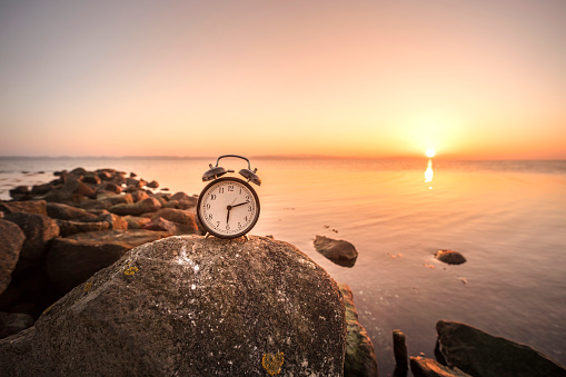 Alarm clock in the sunrise by the sea on a large rock by the shore
