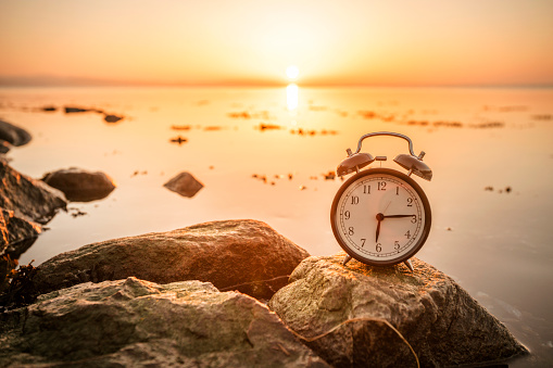 Alarm clock on a rock in the sunrise by the ocean in the morning