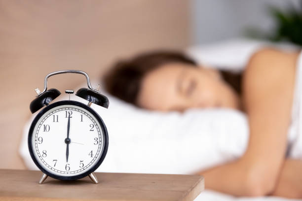 reloj despertador en la mesita de noche con la mujer durmiendo sobre el fondo - sleeping fotografías e imágenes de stock