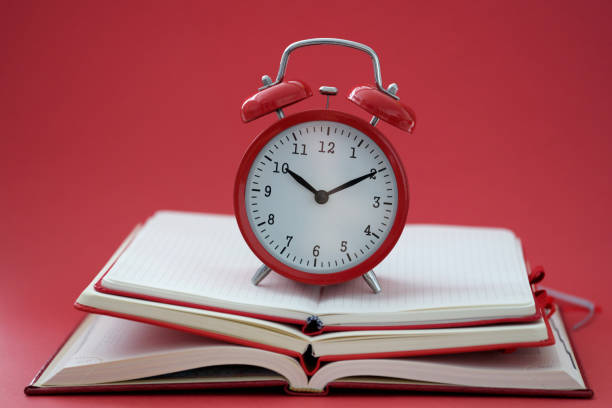 Alarm clock standing on pile of books on red background closeup stock photo