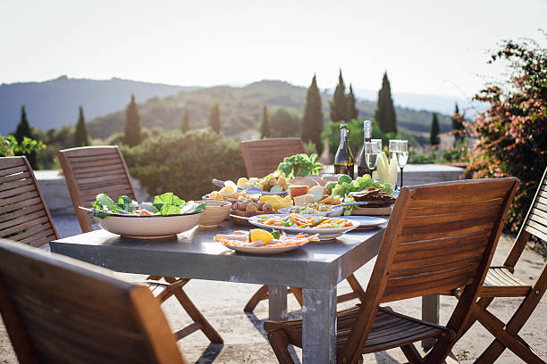 A horizontal image of a typical outdoor Mediterranean meal, there is a beautiful landscape of Tuscany, Italy, in the background. There are no people in the shot.