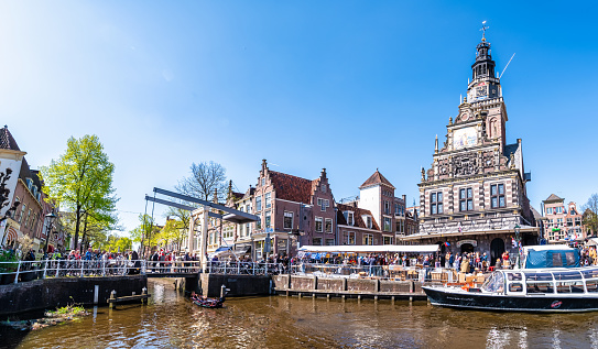 April 22, 2022 - Alkmaar, The Netherlands: nautical vessel in the canal in front of Alkmaar Cheese Market and old Church converted in to a museum and market building