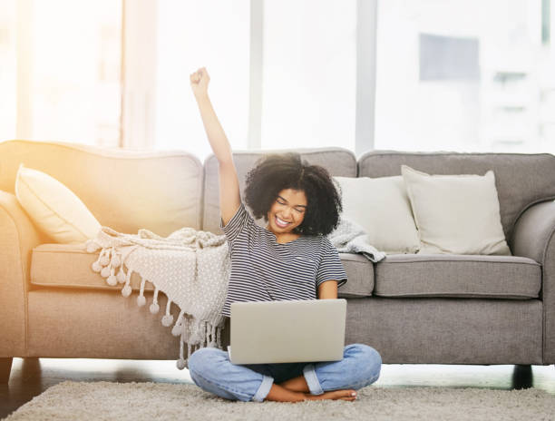 All those online competitions paid off Shot of an attractive young woman using a laptop and cheering at home good news stock pictures, royalty-free photos & images