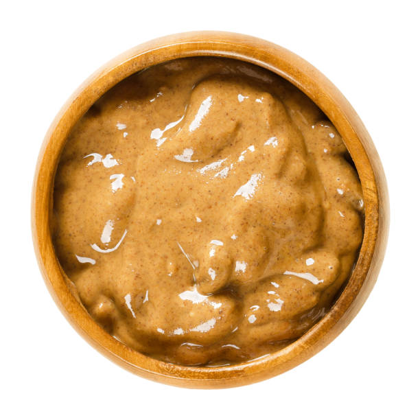 Almond butter in wooden bowl over white Almond butter in wooden bowl. Smooth brown food paste made of almonds. Puree of the nuts of Prunus dulcis. Isolated macro food photo close up from above on white background. almond butter stock pictures, royalty-free photos & images