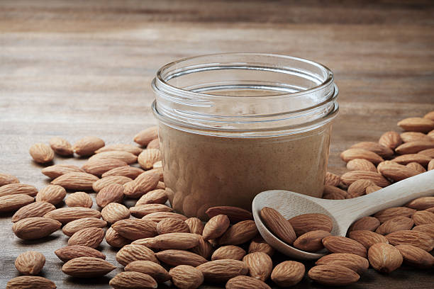 Almond Butter A jar of almond butter and a scoop surrounded by a bed of almonds. almond butter stock pictures, royalty-free photos & images