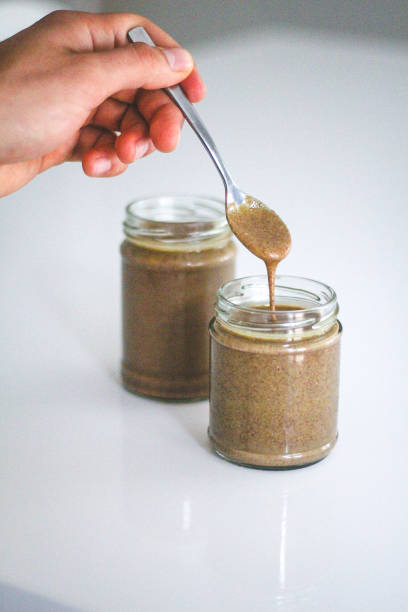 Almond butter with spoon and hand Hand holding spoon dripping homemade almond butter into jar almond butter stock pictures, royalty-free photos & images