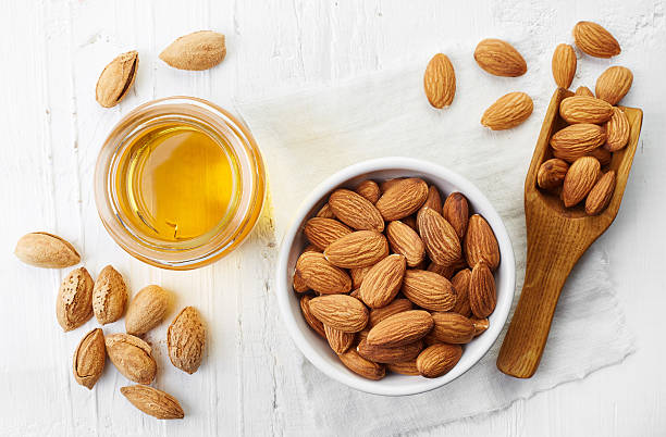 Almond oil and almonds Almond oil and bowl of almonds on white wooden background. Top view almond stock pictures, royalty-free photos & images