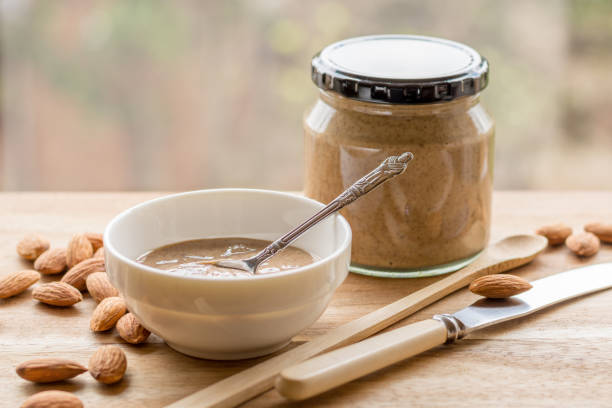 Almonds and Almond Nut Butter Homemade Almond Nut Butter in a jar and small bowl, with almonds on wooden board almond butter stock pictures, royalty-free photos & images