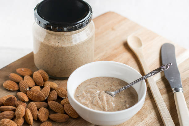 Almonds and Almond Nut Butter Homemade Almond Nut Butter in a jar and small bowl, with almonds on wooden board almond butter stock pictures, royalty-free photos & images