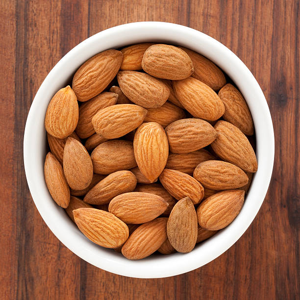 Almonds Top view of white bowl full of almonds almond stock pictures, royalty-free photos & images