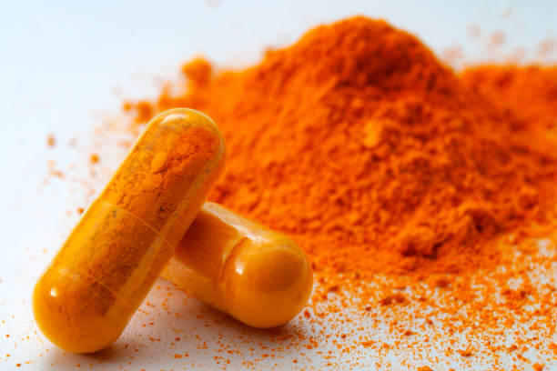 Alternative medicine, antioxidant food and herbal remedy concept theme with macro close up on supplement pill of  curcumin or turmeric with a heap of the spice in dry powder form in the background stock photo