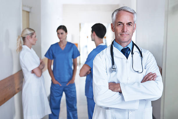Portrait of a mature male doctor with hospital staff standing in the...