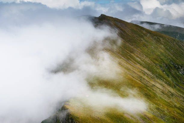 Photo of Amazing landscape of summer mountains. View of fog and low clouds over Fagaras Mountains are the highest mountains of the Southern Carpathians. Romania. Travel background.