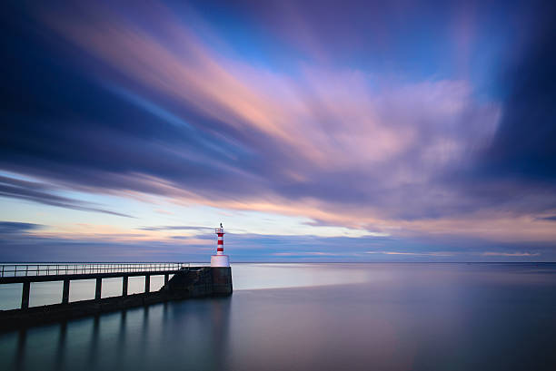 Amble pier and lighthouse at sunset long exposure Amble pier and lighthouse in Northumberland at sunset using a long exposure to produce streaks in the clouds and smooth blurred sea water northumberland stock pictures, royalty-free photos & images