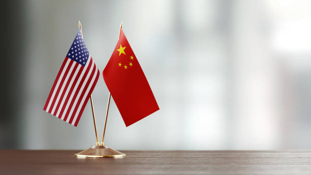 American and Chinese flag pair on desk over defocused background. Horizontal composition with copy space and selective focus.