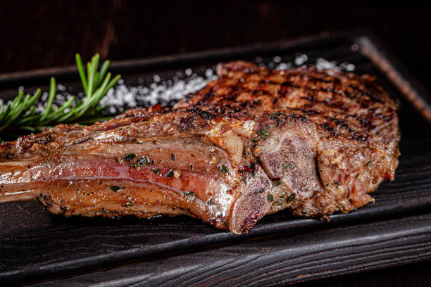 American cuisine. Large juicy grilled steak on a tomahawk bone. Beef steak on a wooden board with rosemary and salt. background image, copy space text stock photo