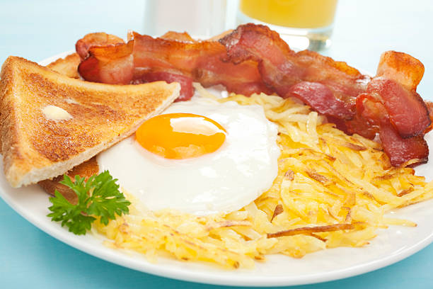 American English Breakfast Hash Browns Bacon Fried Egg Toast "Cooked breakfast of crisply fried bacon, fried egg sunny side up, hash browns, toast and orange juice. More breakfasts:-" hash brown stock pictures, royalty-free photos & images