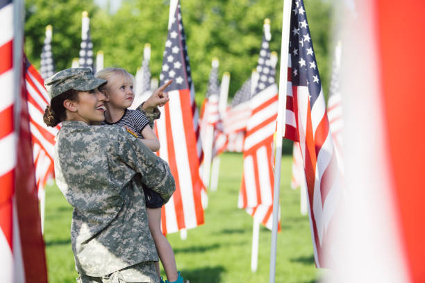 American female soldier with 3 year old girl American female soldier in uniform in a field of flags with a little blonde girl. memorial day stock pictures, royalty-free photos & images