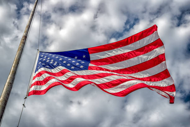 American Flag at Half-Staff American flag at half-mast or half-staff blowing in wind with blue sky and clouds. flag at half staff stock pictures, royalty-free photos & images