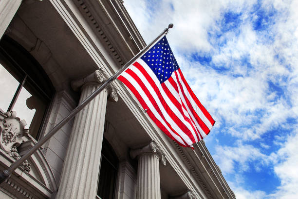 American flag flying over government building in city, blue sky and clouds stock photo